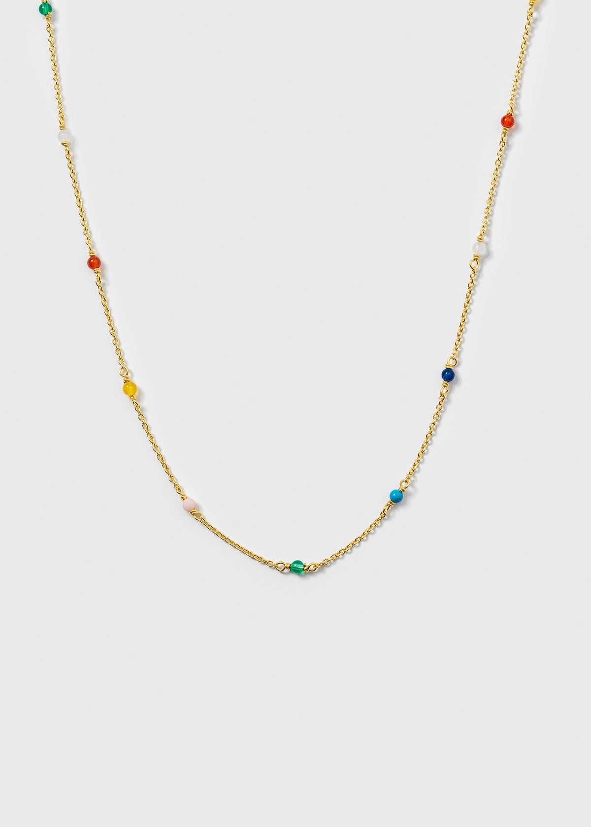 A product shot of the Santa Monica Necklace in gold, laid out to display its design of a fine chain adorned with small, colorful gemstones: Yellow Jade, Pink Opal, Sodalite, Green Onyx, Blue Color Reconstituted Turquoise, White Agate, and Carnelian.