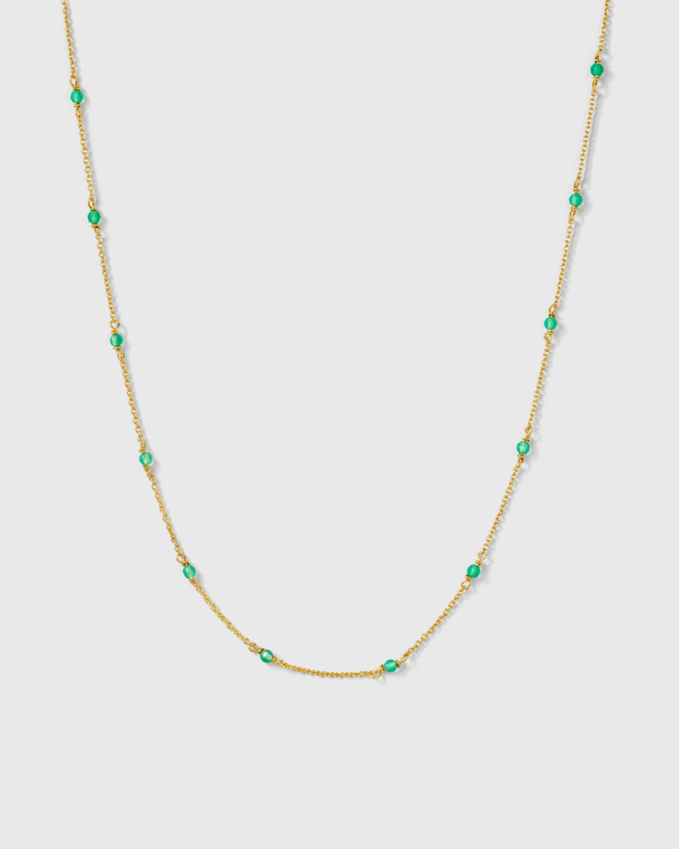 A product shot of the Santa Monica Necklace in gold, featuring a fine chain adorned with small, vibrant green onyx stones spaced evenly along its length.