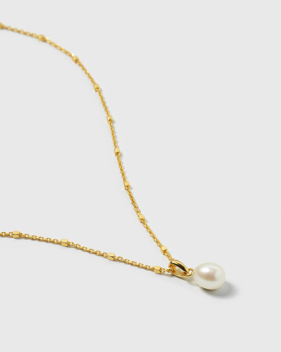 A close-up product shot of the Treasure Single Pearl Necklace in gold, showing its delicate, beaded chain and the single freshwater pearl pendant.