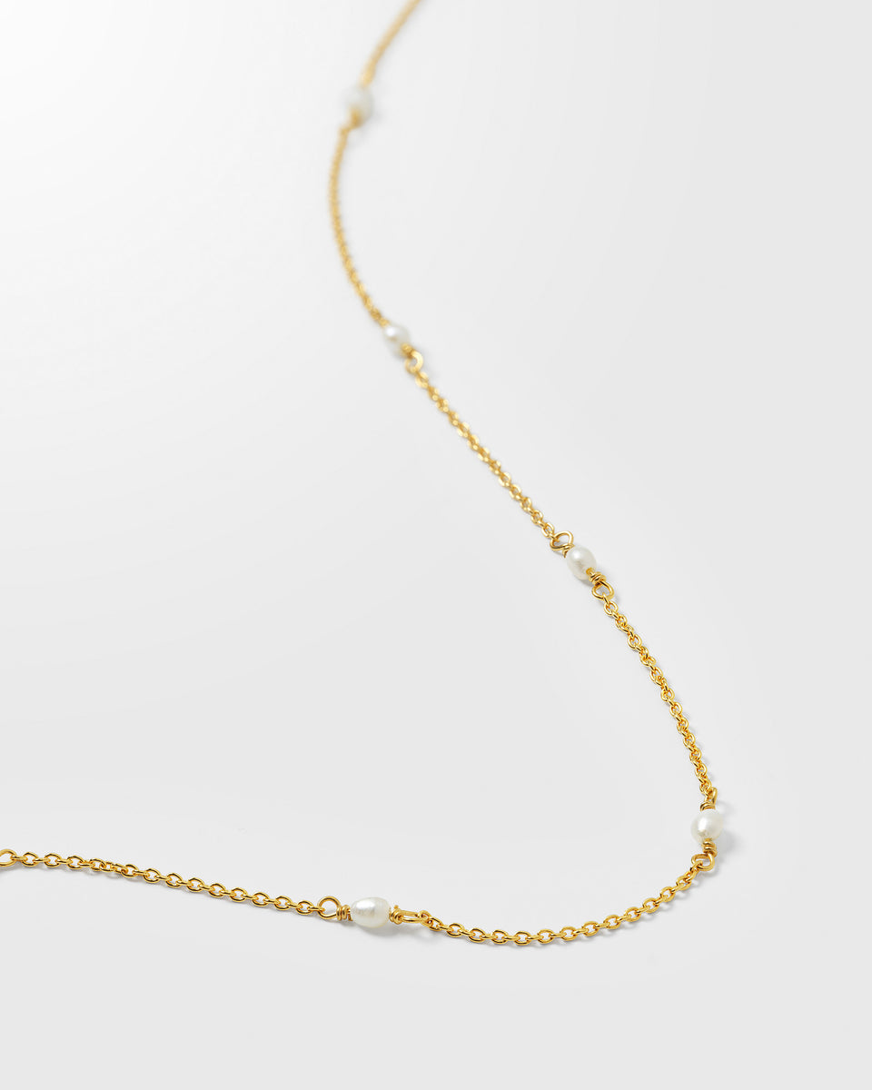 A close-up image of the Treasure Multi Pearl Necklace in gold, detailing the delicate chain and the small freshwater pearls set along its length.