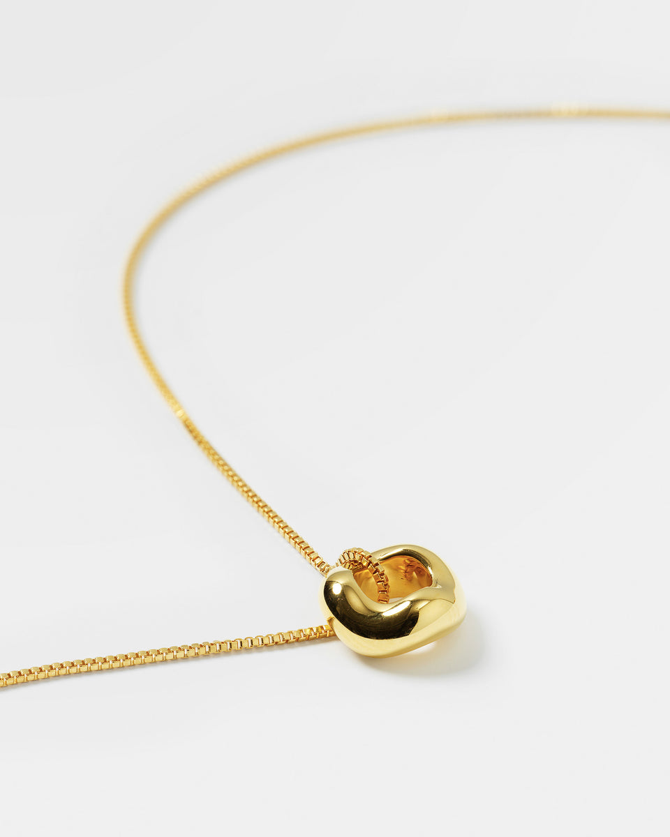 A product shot of the Bolded Wavy Necklace in gold, featuring a smooth box chain and a shiny, chunky pendant with a soft, wavy design.