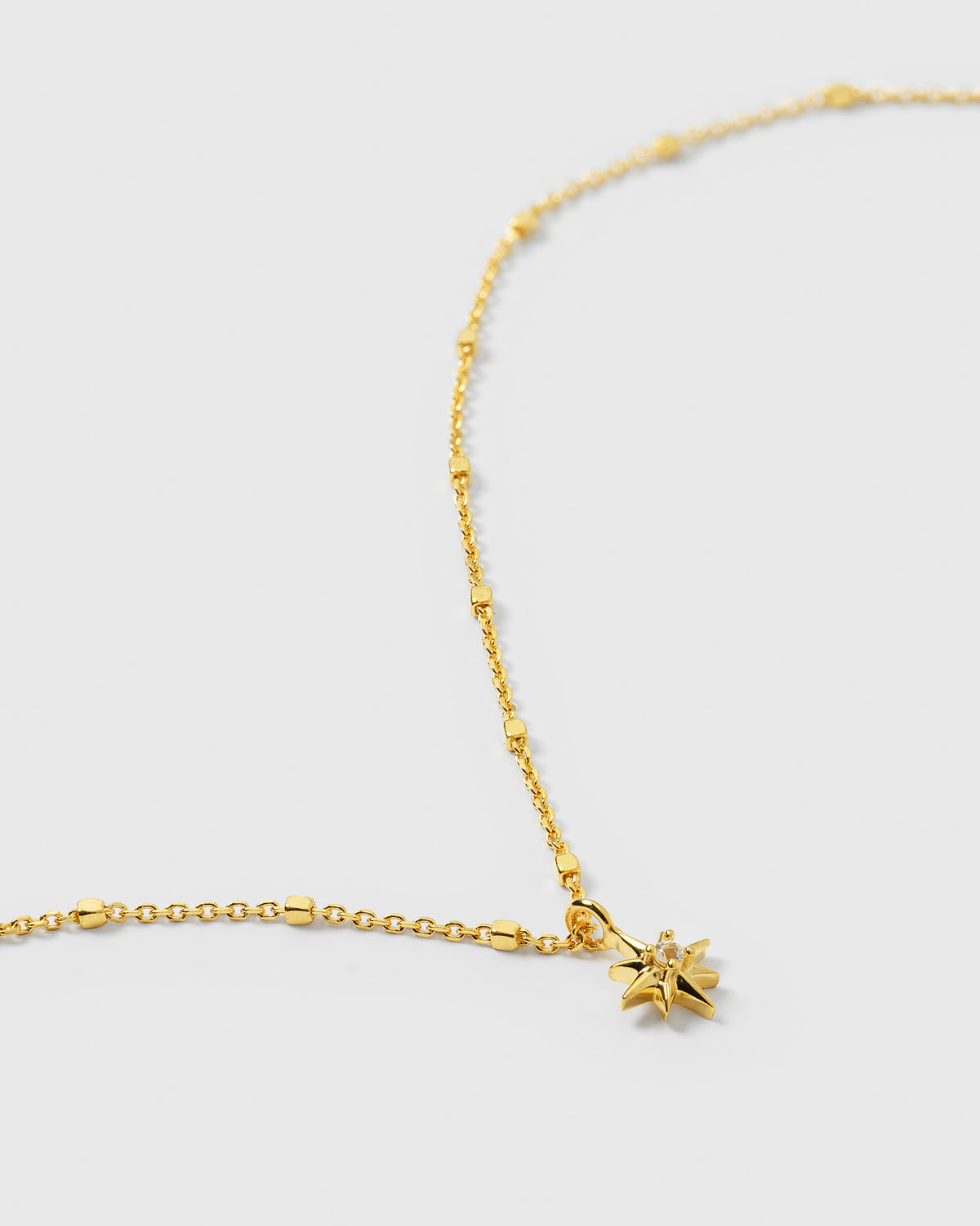 A product shot of the North Star Necklace in gold, showing a close-up of the star-shaped pendant with a central crystal and its unique beaded chain.