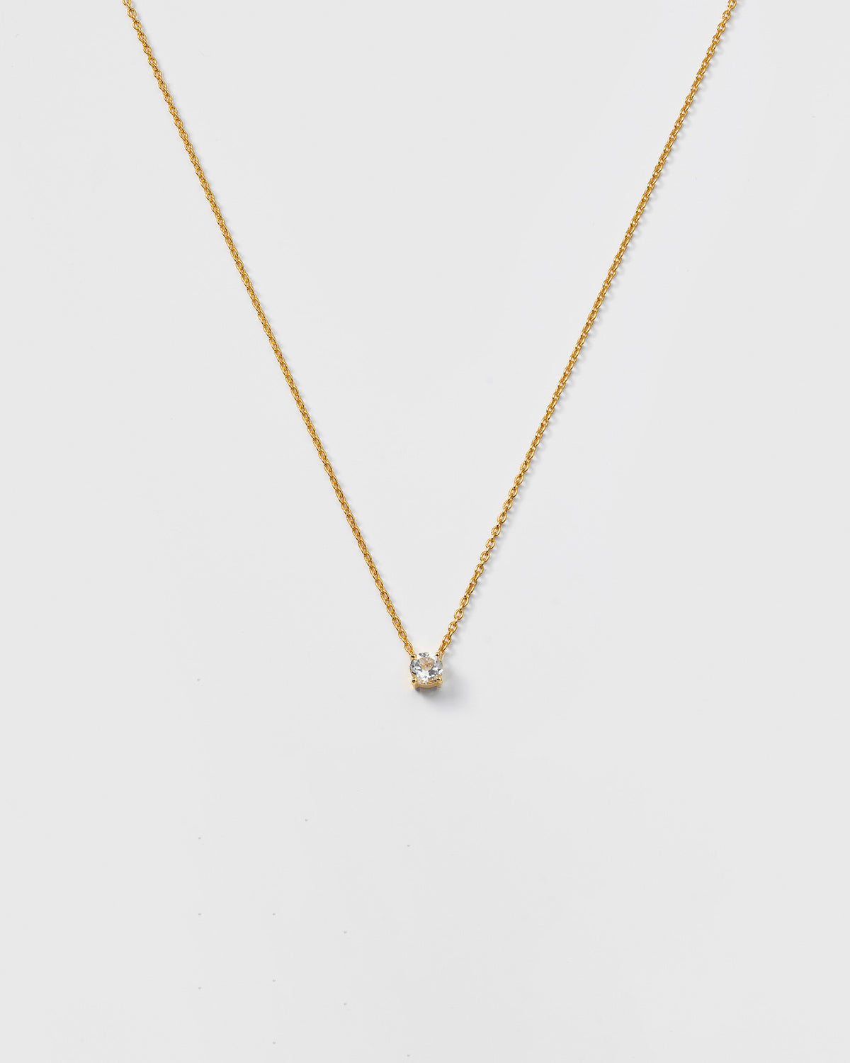 A product shot of the Minimalistica Solo Nova Necklace in gold, featuring a delicate chain with a small, round white topaz stone at the center.