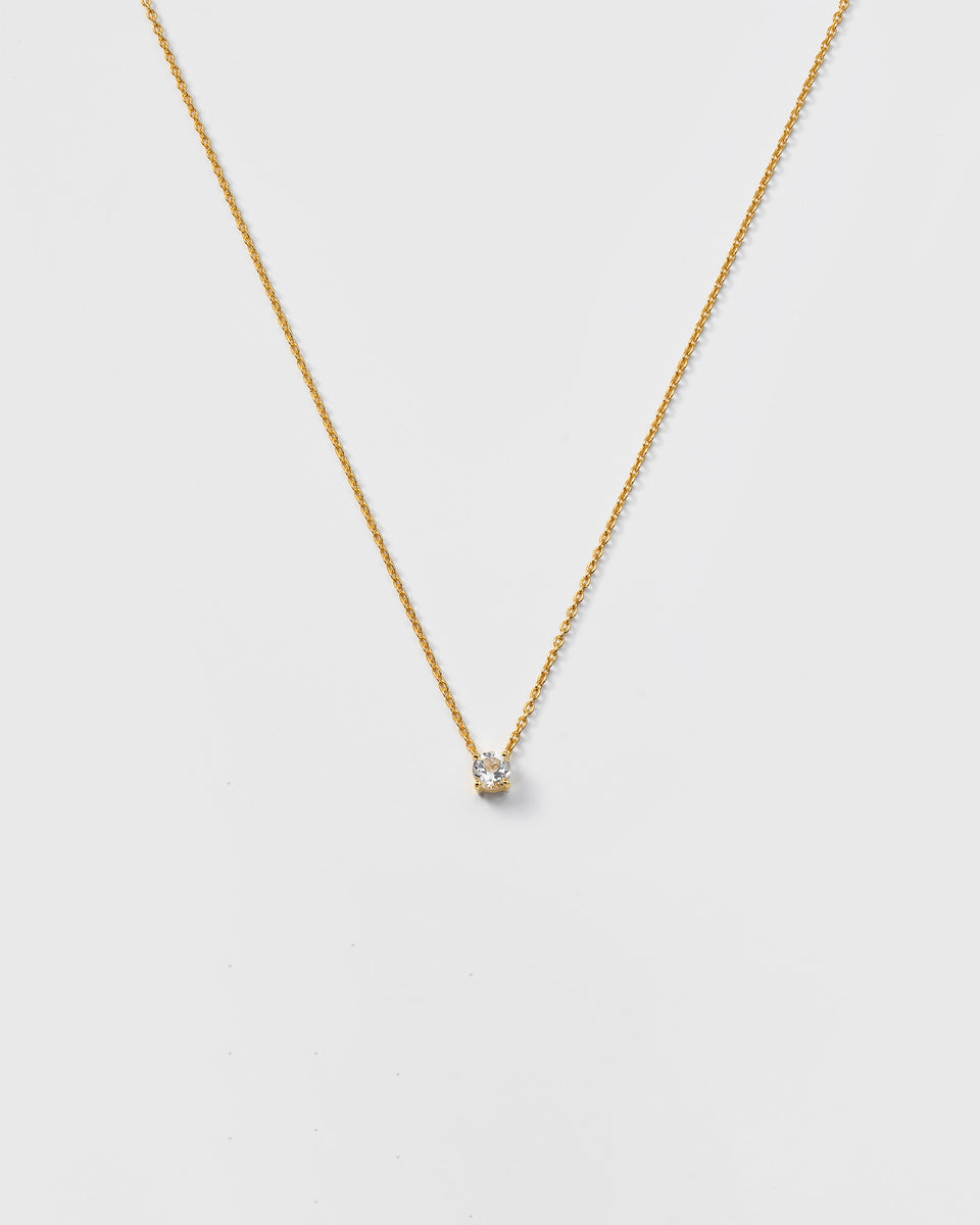 A product shot of the Minimalistica Solo Nova Necklace in gold, featuring a delicate chain with a small, round white topaz stone at the center.