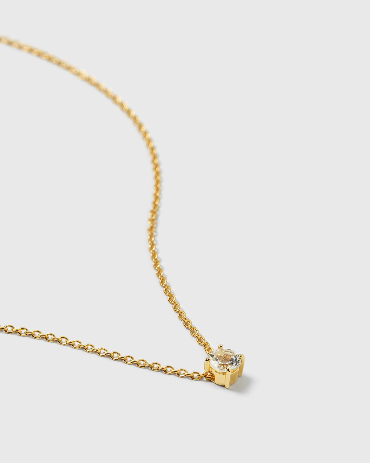 A close-up shot of the Minimalistica Solo Nova Necklace in gold, showcasing the delicate chain and its small, round white topaz in a four-prong setting.
