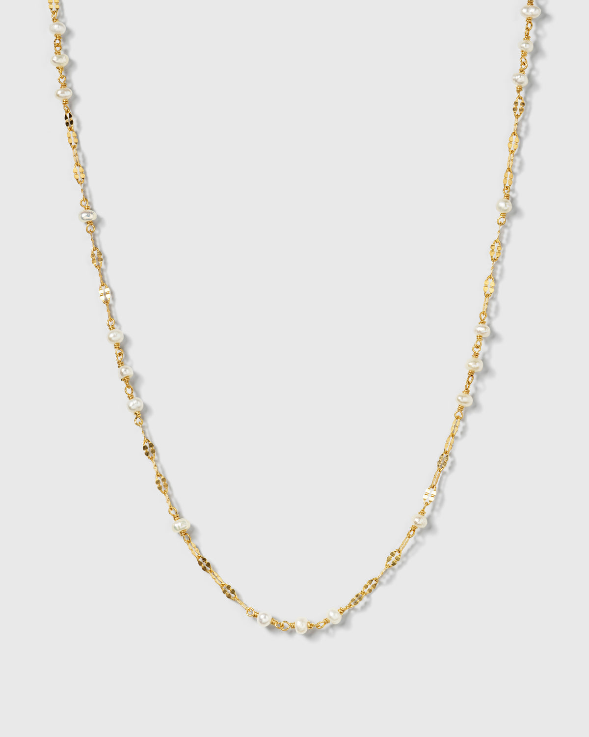 A product shot of the Aurelia Necklace Gold, featuring a unique patterned gold chain interspersed with small freshwater pearls.