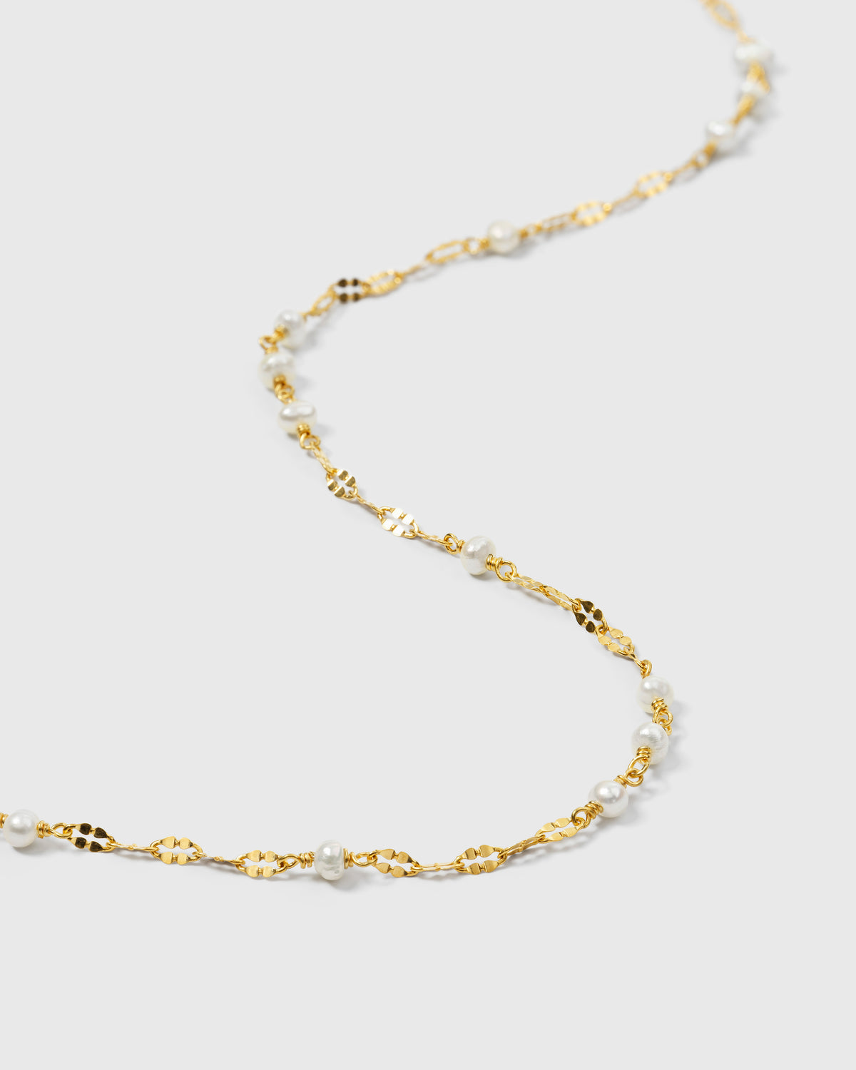 A close-up shot of the Aurelia Necklace in gold, showcasing its unique chain of patterned links interspersed with small freshwater pearls.