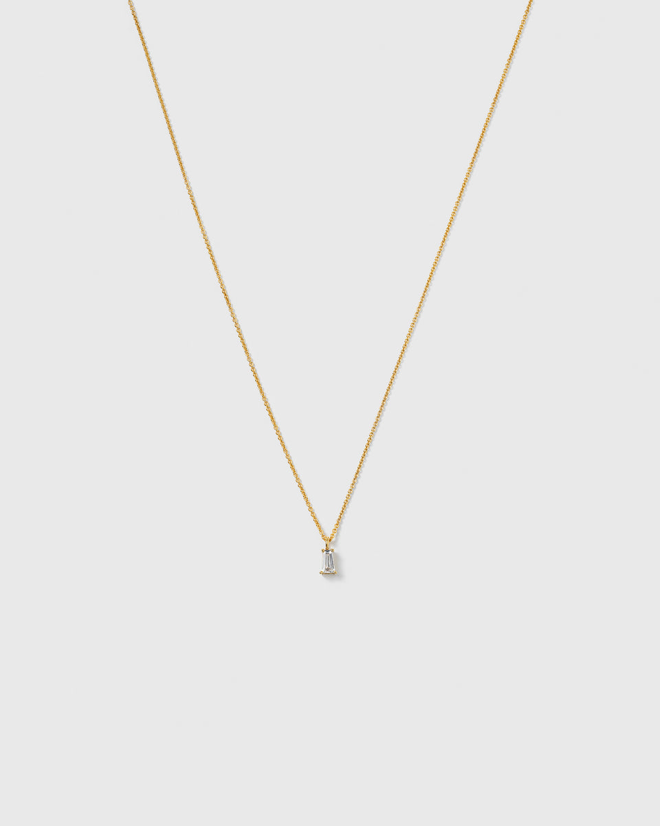 A product shot of the Iggy Necklace Gold, featuring a delicate gold chain and a single pendant with a tapered baguette-cut cubic zirconia.