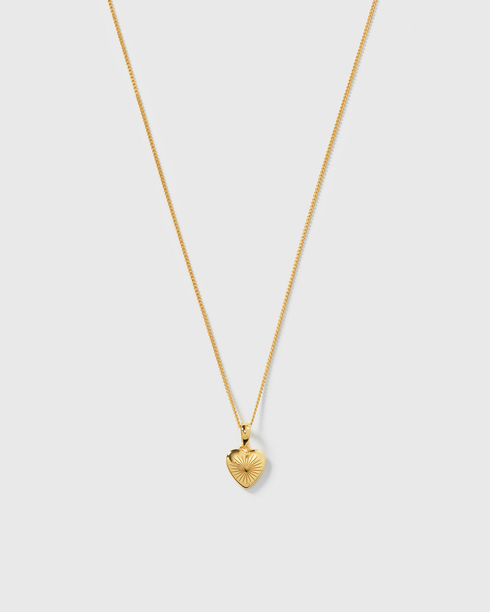 A product shot of the Sunburst Heart Necklace in gold, featuring a fine chain and a heart-shaped pendant with an engraved sunburst pattern.