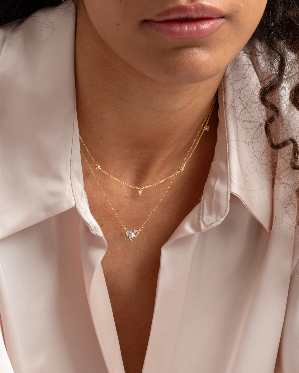 A close-up of a model wearing the Celestia Necklace in gold, featuring a delicate chain with sparkling, varied cubic zirconia stones, layered with another gold necklace.