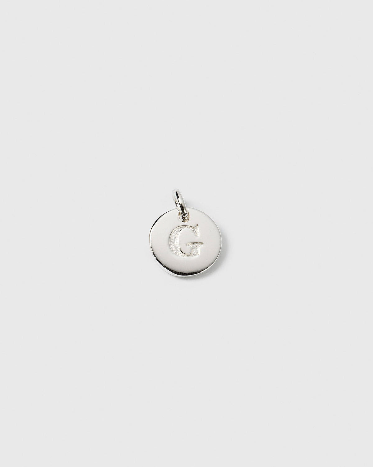 A product shot of the silver Beloved Mini Letter G pendant, showing the initial engraved on a small, circular charm.