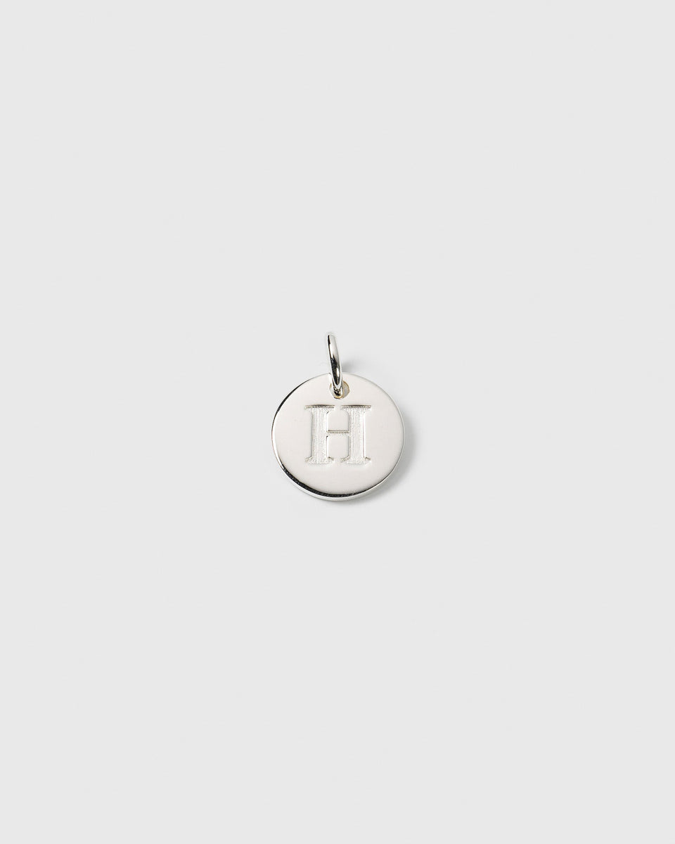 A product shot of the Beloved Mini Letter charm in silver, featuring the initial 'H' engraved on a small, round pendant.