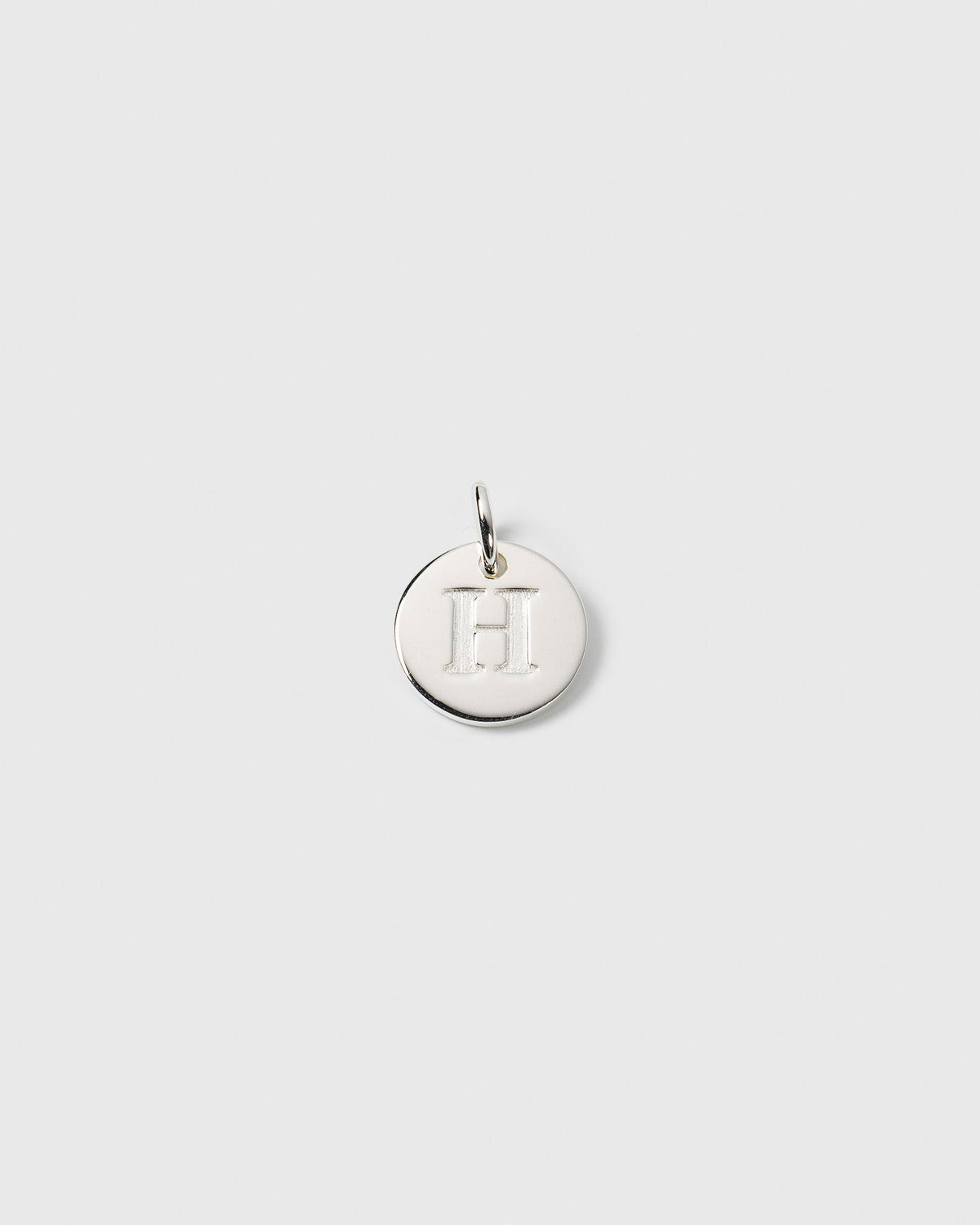 A product shot of the Beloved Mini Letter charm in silver, featuring the initial 'H' engraved on a small, round pendant.