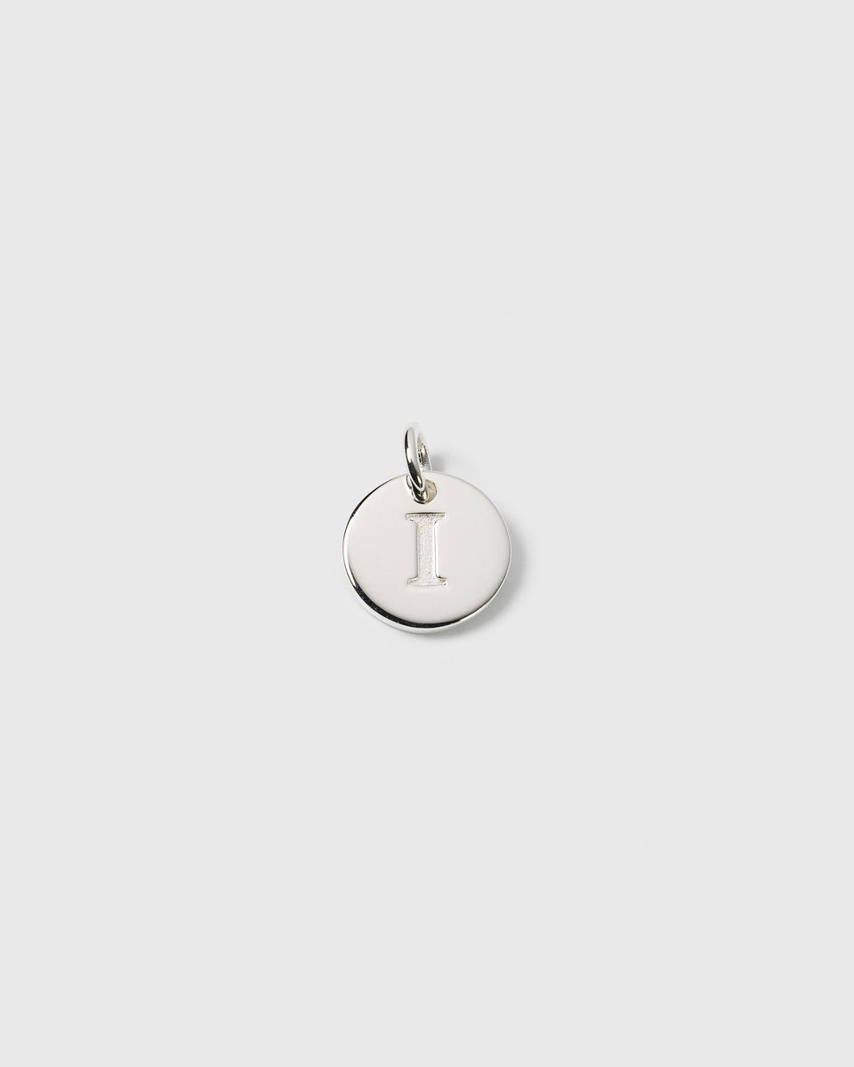 A product shot of the Beloved Mini Letter pendant in silver, a round charm featuring the engraved letter 'I'.
