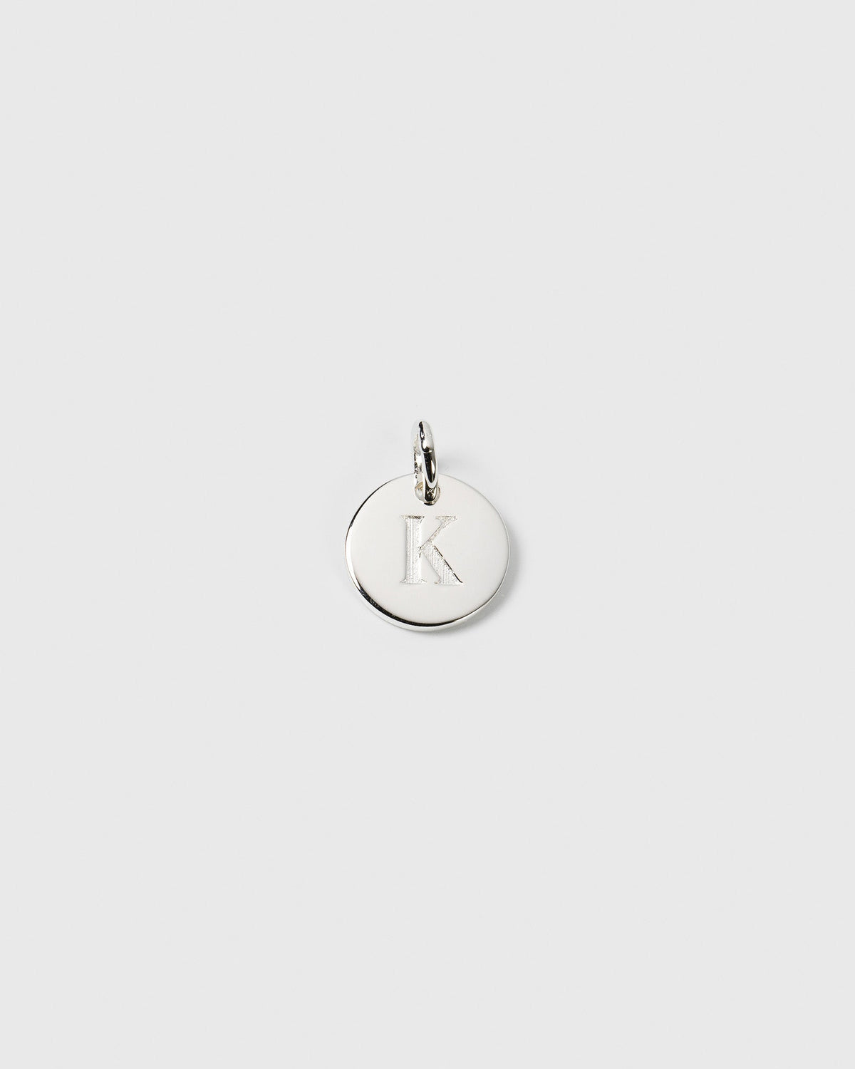 A product shot of the Beloved Mini Letter charm in silver, featuring a round disc with the letter 'K' engraved on it.