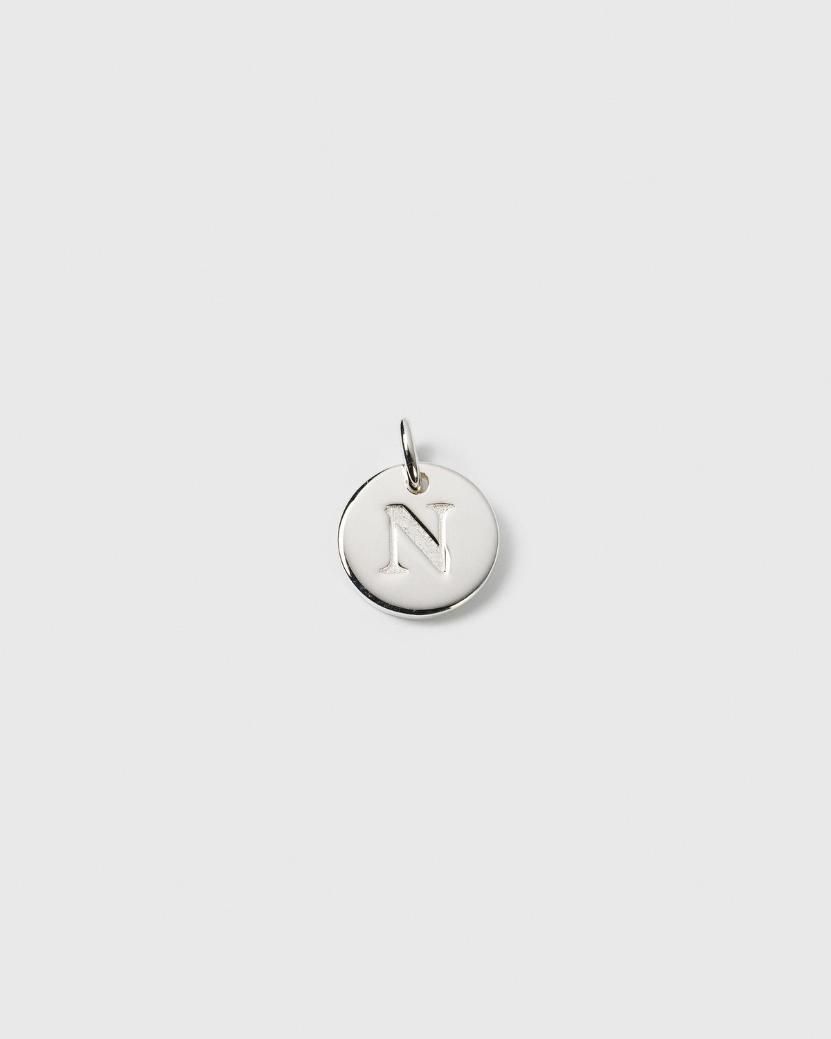 A product shot of the Beloved Mini Letter Silver pendant, featuring a small, circular silver charm with the letter 'N' engraved in the center.