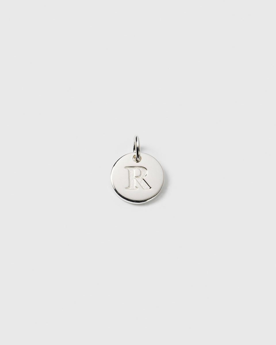 A product shot of the Beloved Mini Letter R pendant in silver, showcasing the letter 'R' engraved on the small, round charm.