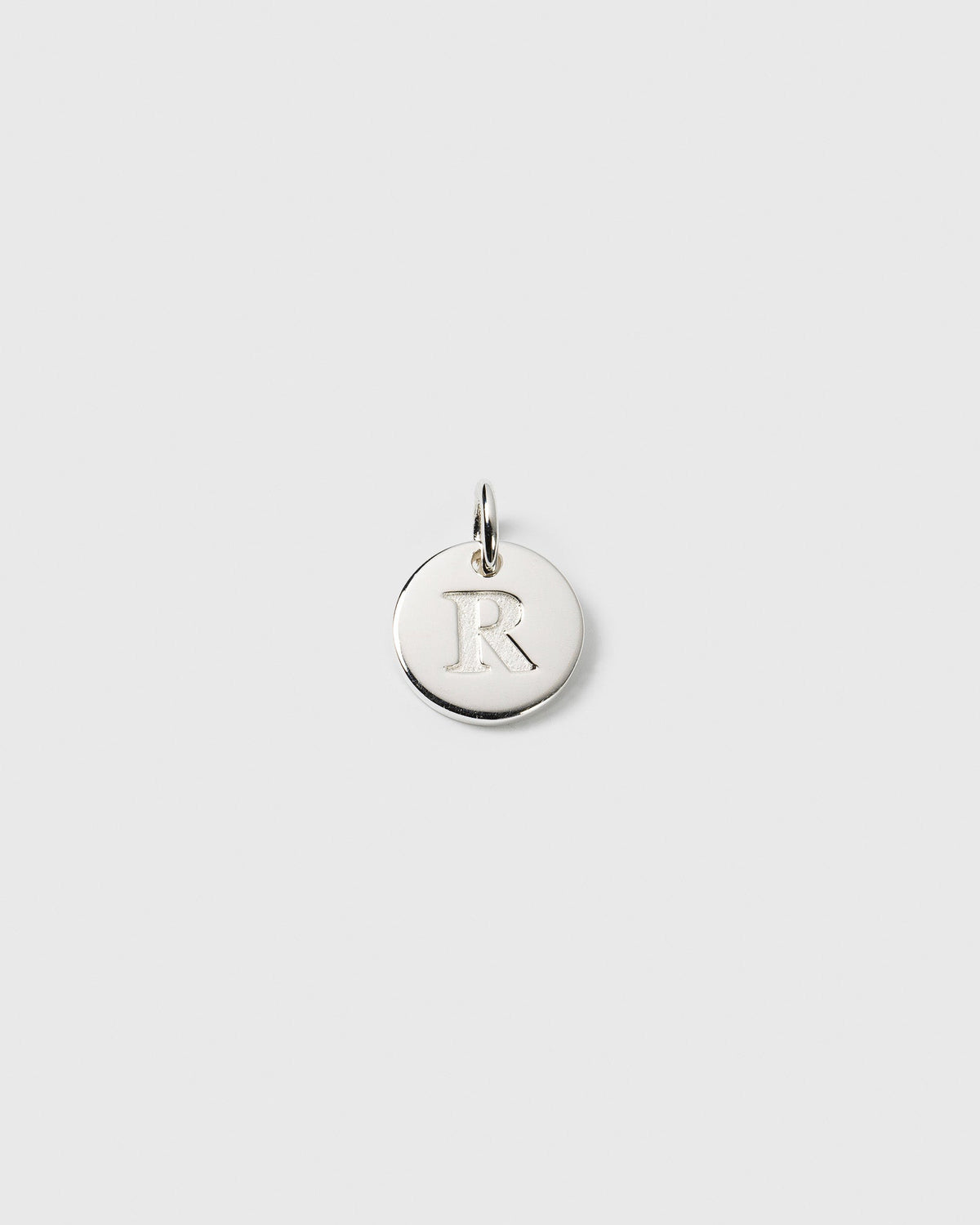 A product shot of the Beloved Mini Letter R pendant in silver, showcasing the letter 'R' engraved on the small, round charm.