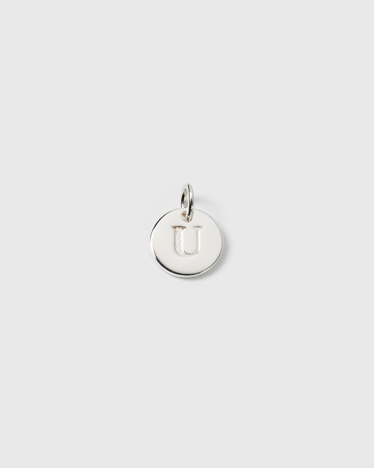 A product shot of the Beloved Mini Letter Silver pendant, featuring a small, round charm with the letter U engraved on it.