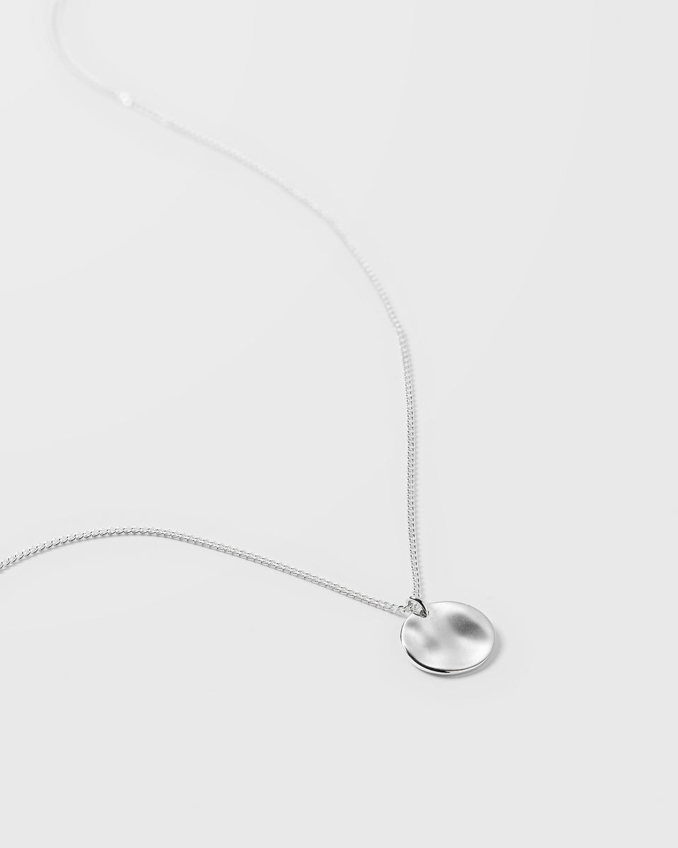 A product shot of the Minimalistica Hammered Necklace in silver, featuring a fine chain and a round, flat pendant with a hammered finish.