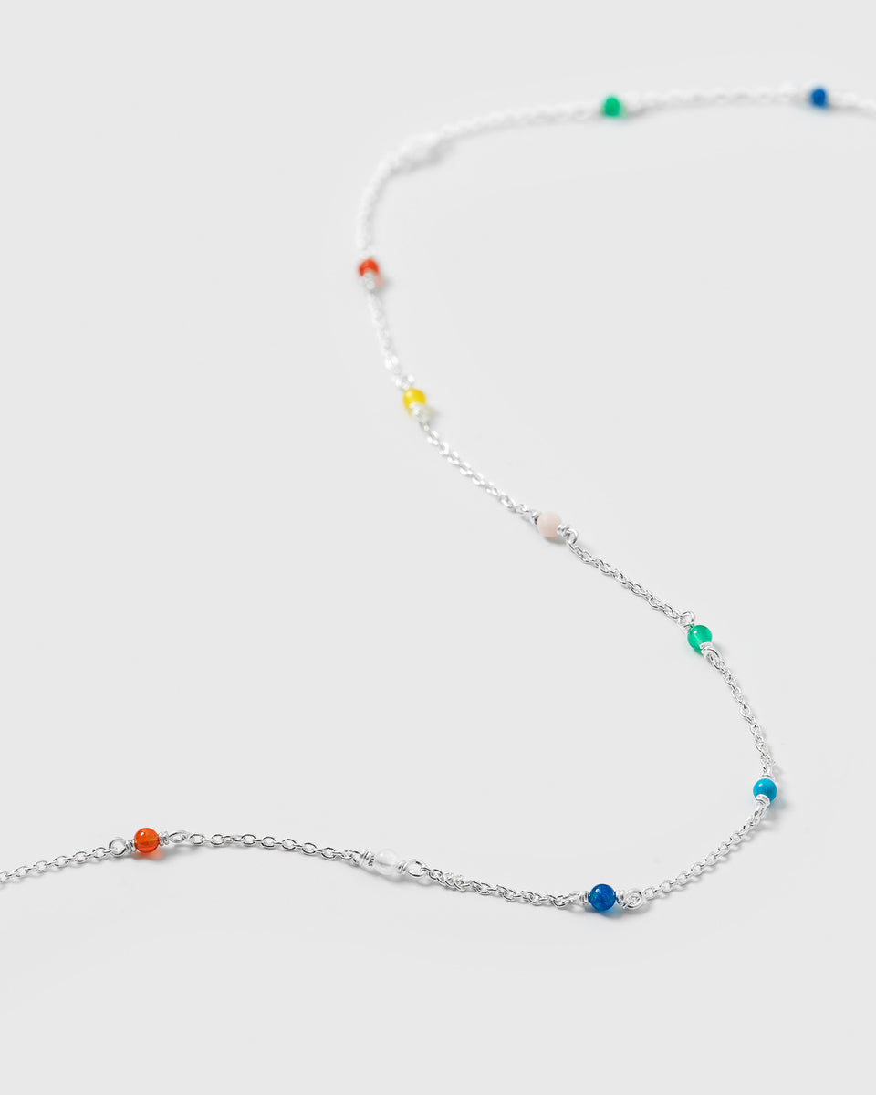 A product shot of the Santa Monica Necklace in silver, laid out to display its fine chain design adorned with small, colorful gemstone beads: Yellow Jade, Pink Opal, Sodalite, Green Onyx, Blue Color Reconstituted Turquoise, White Agate, and Carnelian