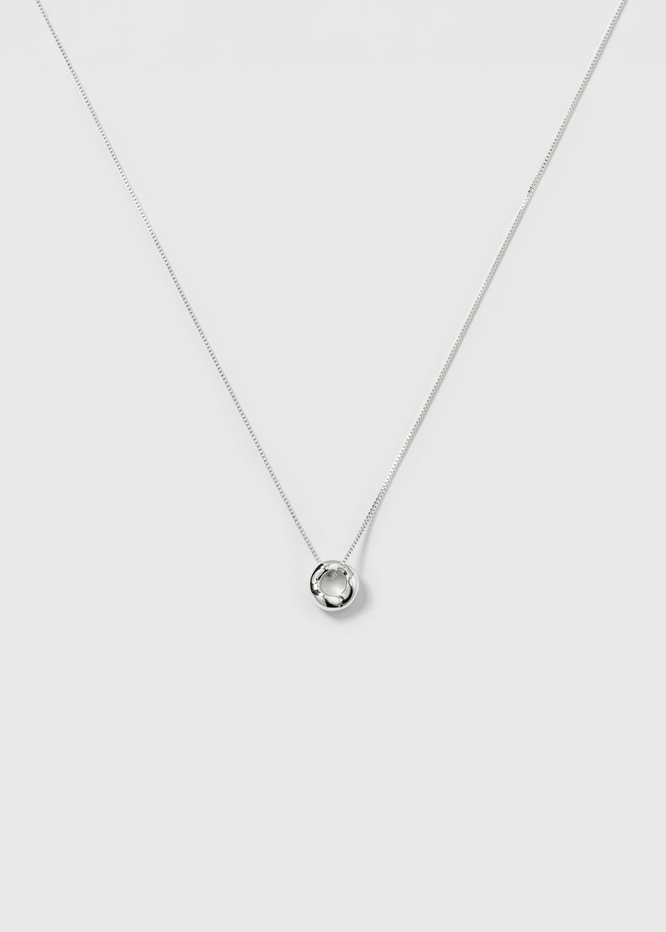 A product shot of the Bolded Wavy Necklace in silver, featuring a smooth chain and a shiny pendant with a wavy, circular design.