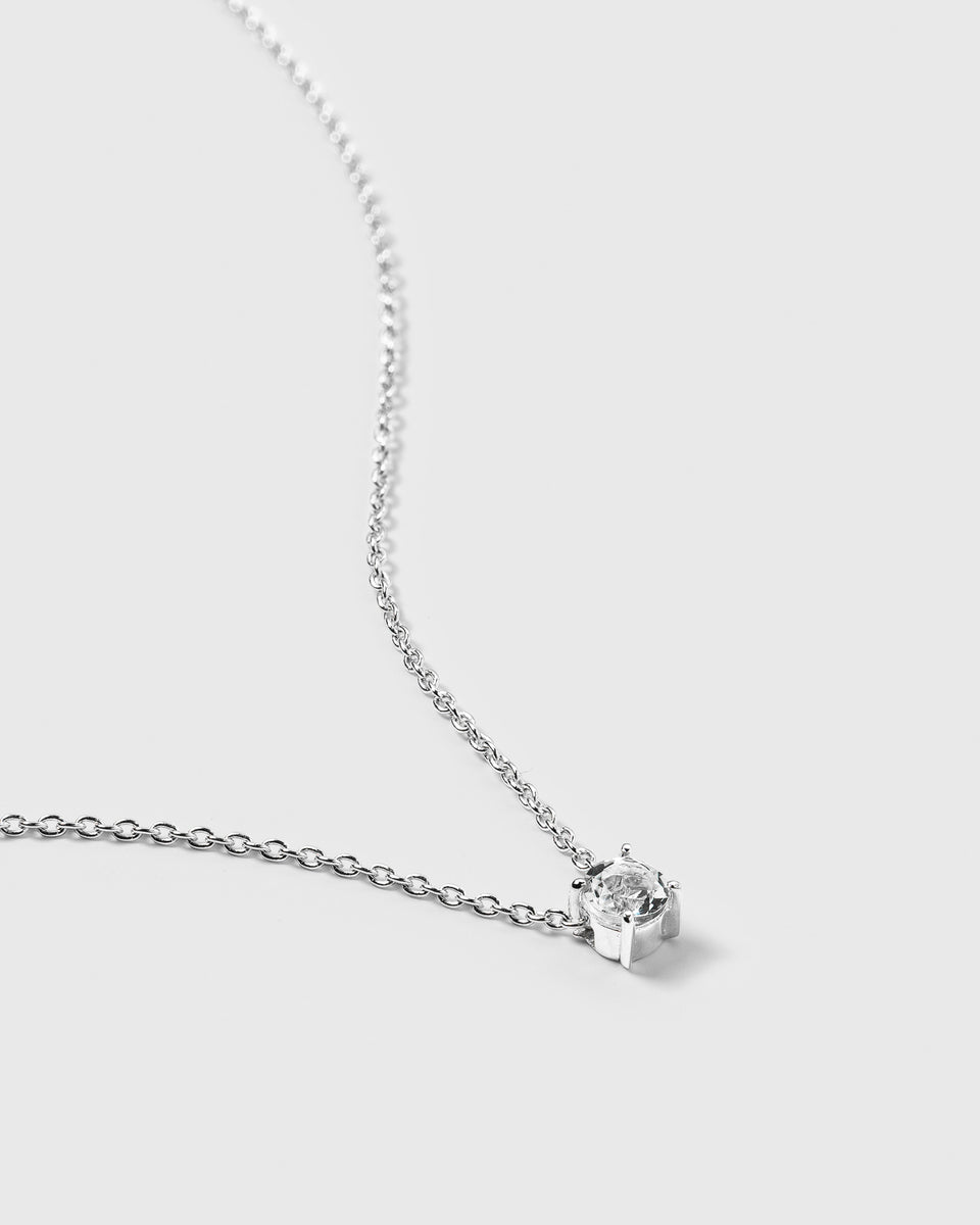 A close-up shot of the Minimalistica Solo Nova Necklace in silver, highlighting its delicate chain and the single white topaz stone set in a prong setting.