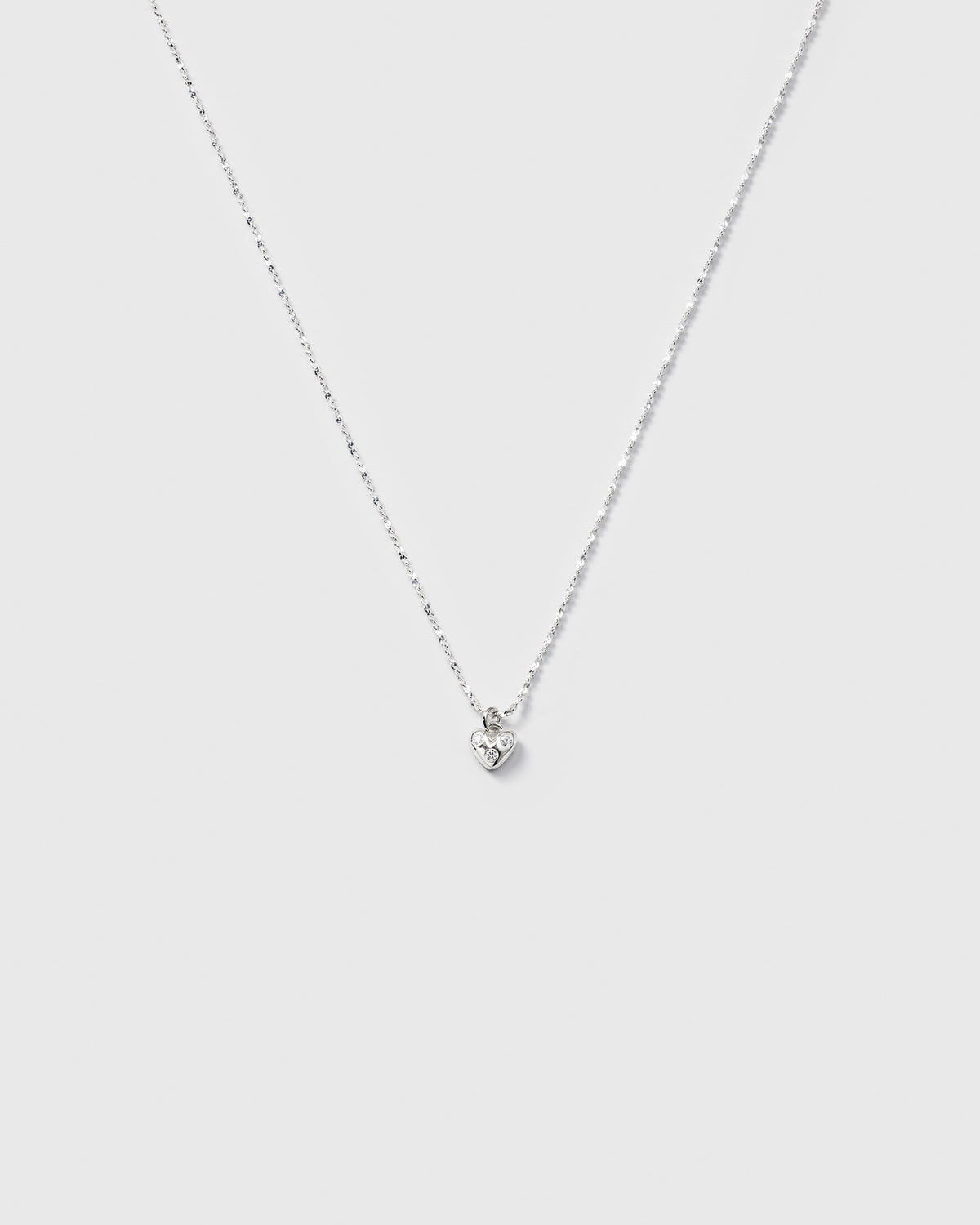 A product shot of the Forever Necklace in silver, showcasing its delicate twisted chain and a small heart pendant set with sparkling cubic zirconia stones.