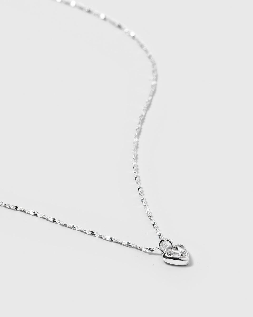 A detailed product shot of the Forever Necklace Silver, showcasing its unique twisted chain and a delicate heart-shaped pendant adorned with sparkling cubic zirconia stones.