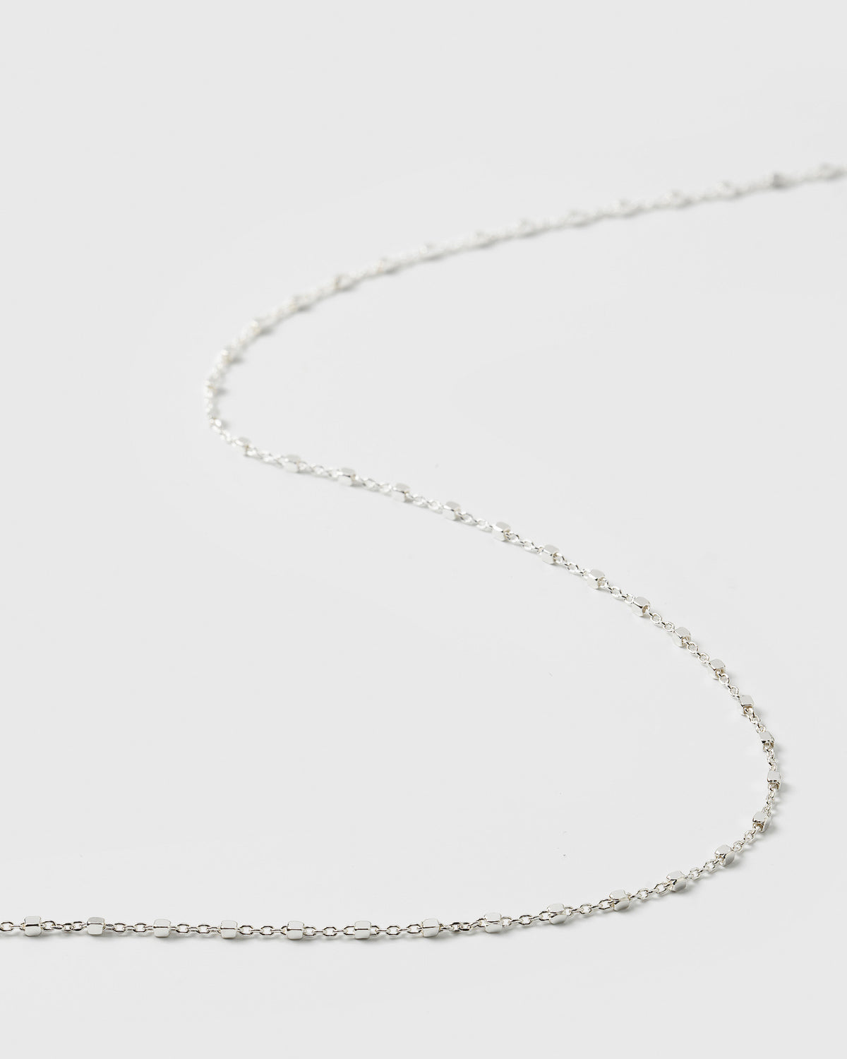 A close-up product shot of the Sheer Station Necklace in silver, highlighting its delicate chain design interspersed with small, shining dots.