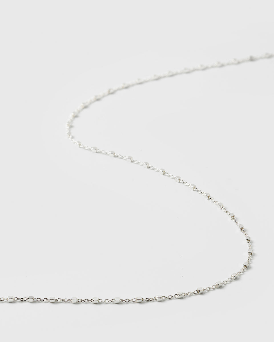 A close-up product shot of the Sheer Station Necklace in silver, highlighting its delicate chain design interspersed with small, shining dots.