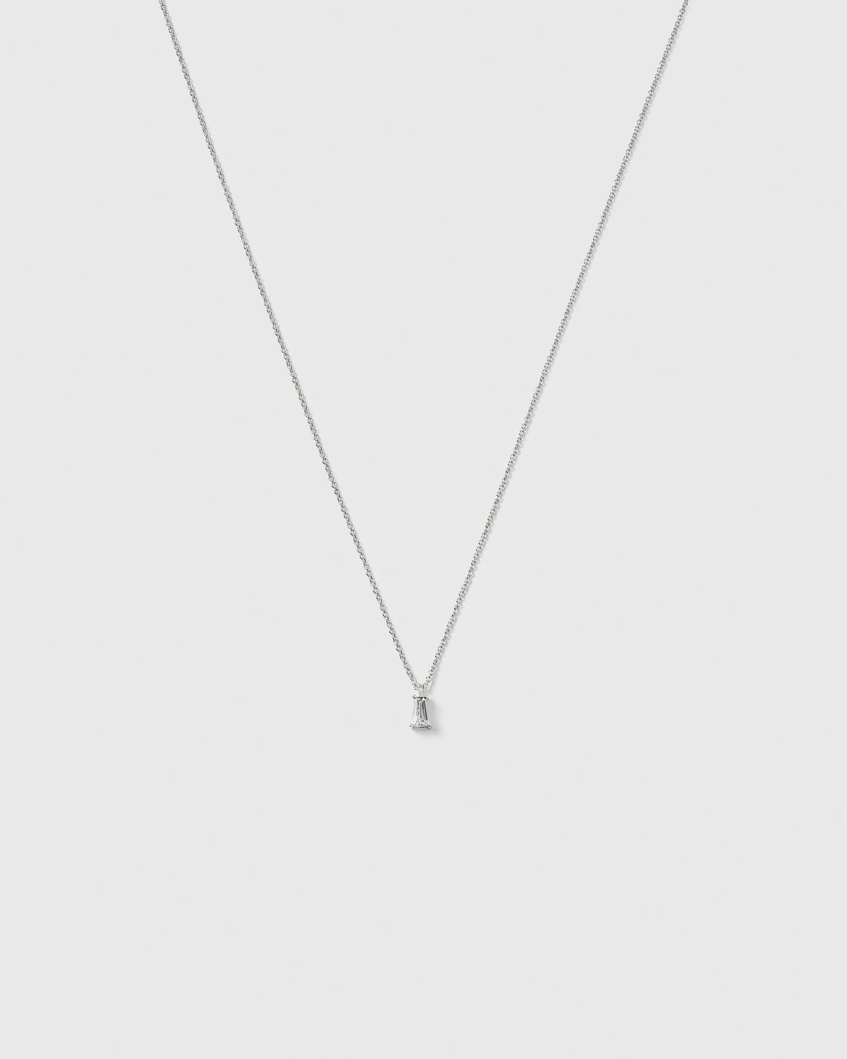 A product shot of the Iggy Necklace in silver, featuring a fine chain and a small pendant with a single, tapered baguette-cut cubic zirconia.