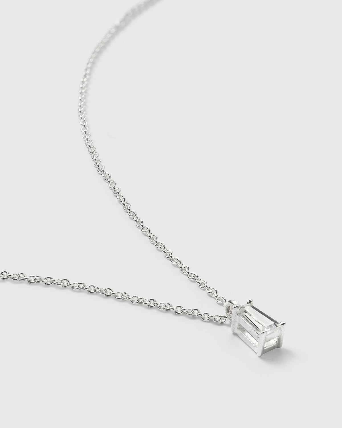 A close-up of the Iggy Necklace in silver, highlighting its delicate chain and the sparkling, tapered baguette-cut cubic zirconia pendant.