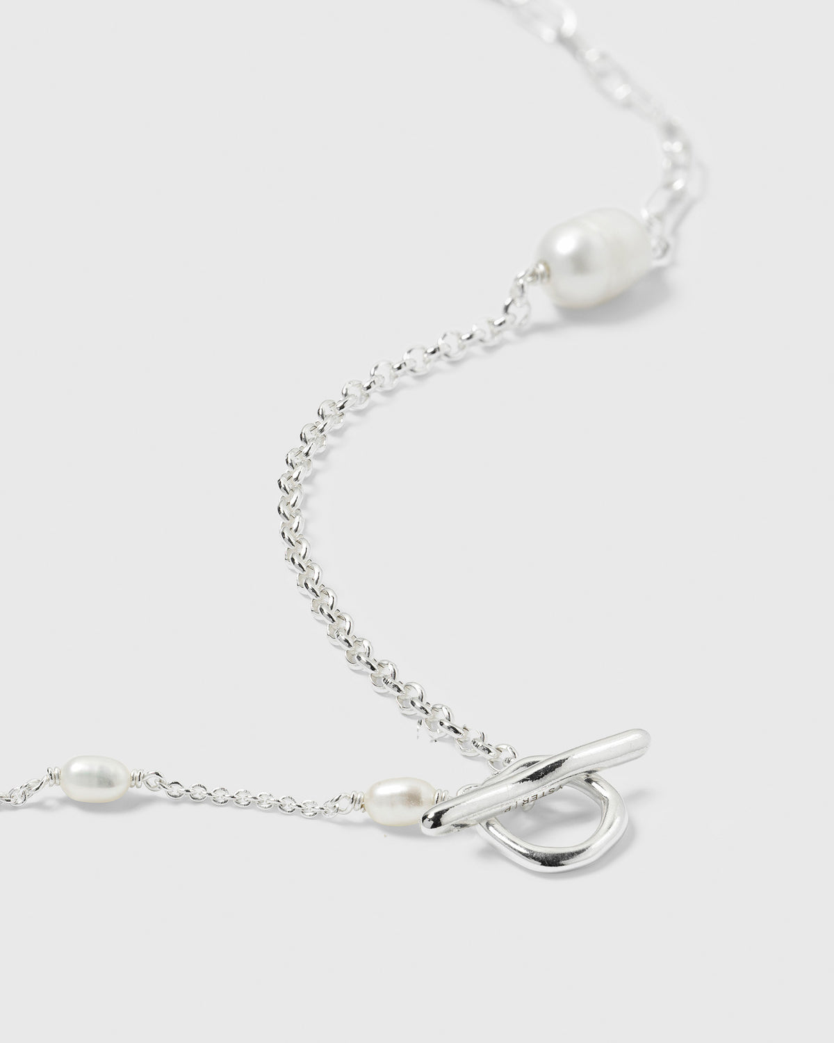 A detailed close-up of the Paxton Short Necklace in recycled sterling silver, showing the toggle clasp, three different chain links, and baroque freshwater pearls.