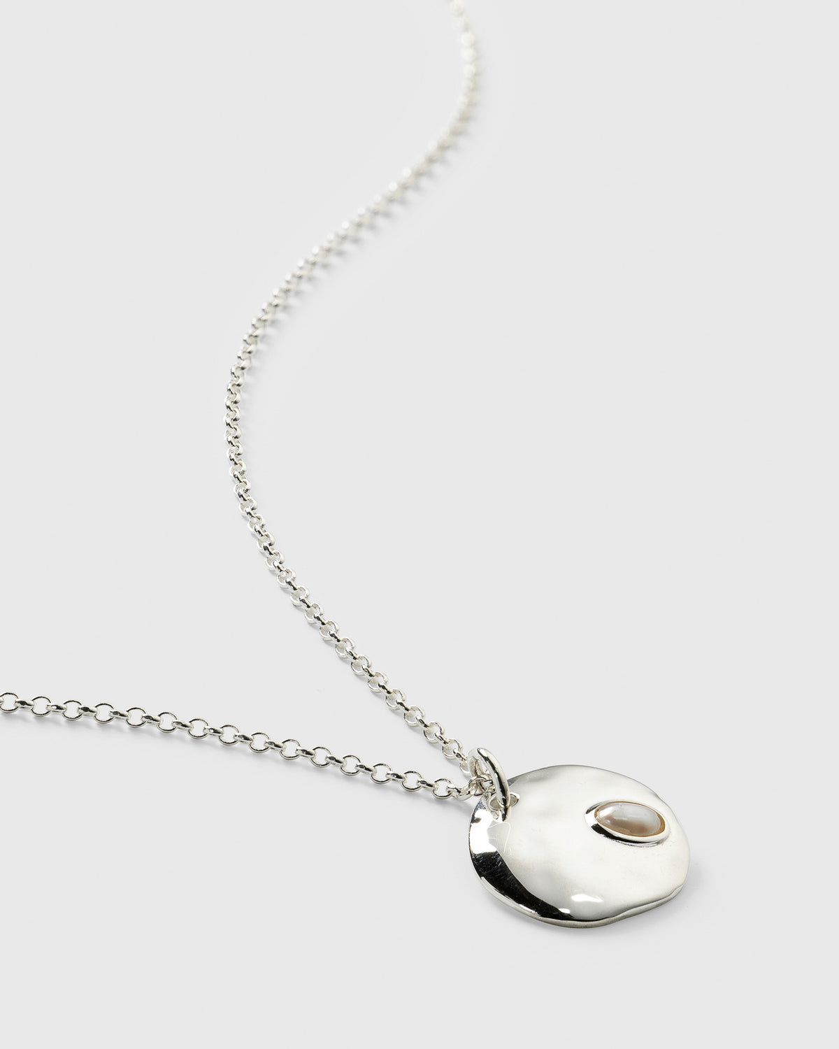 Close-up of the Paxton Necklace in silver, featuring a hammered pendant made of recycled sterling silver with an inset baroque freshwater pearl, on a delicate chain.