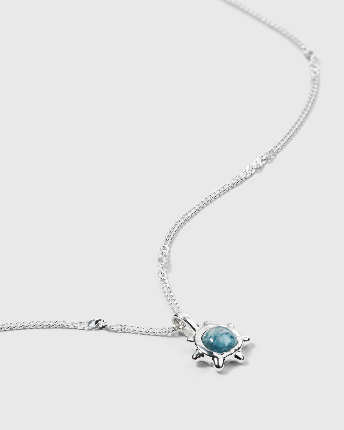 A close-up product shot of the Florentina Necklace in silver, showing the flower-shaped pendant with a central aquamarine stone and its delicate twisted chain.