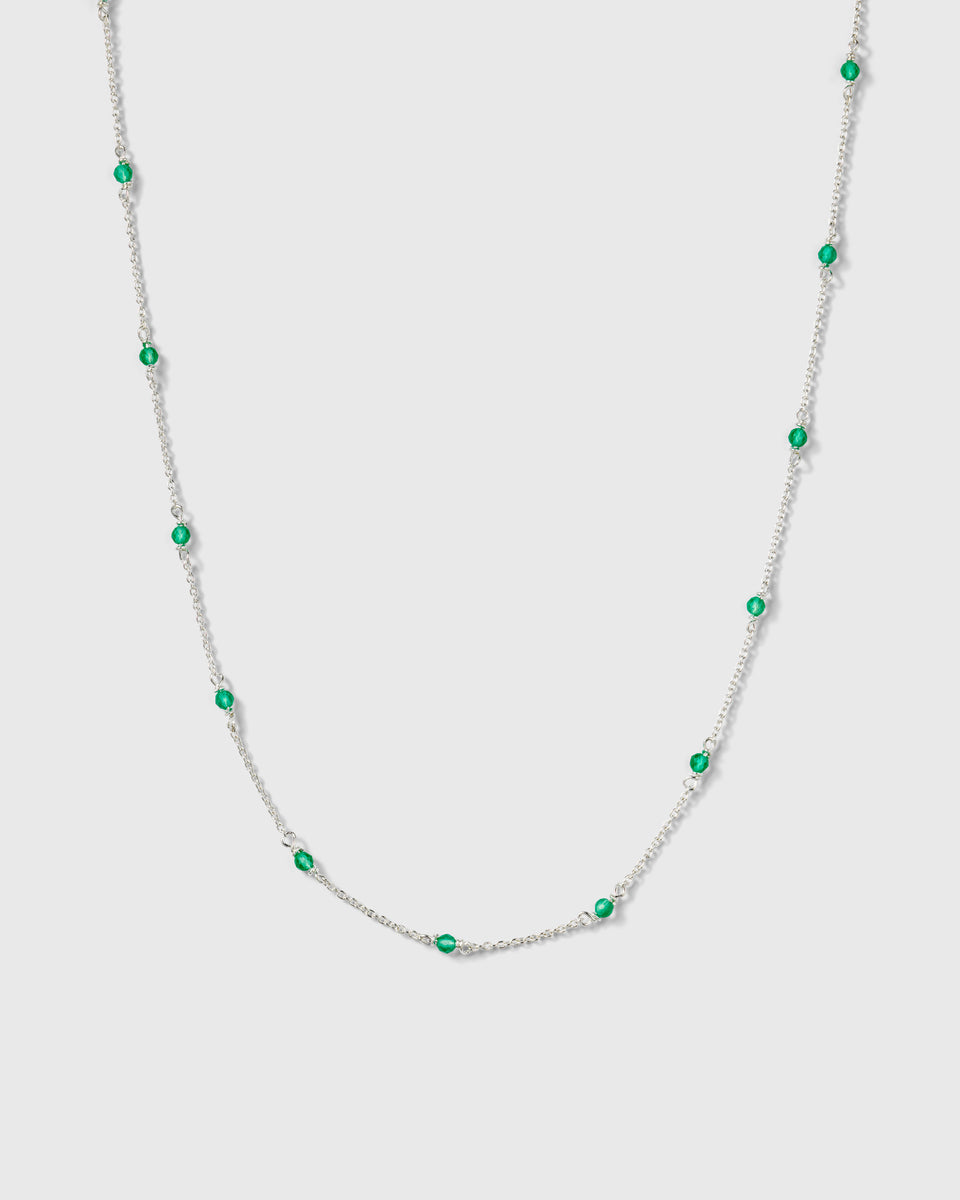 A product shot of the Santa Monica Necklace in silver, featuring a delicate chain with small, vibrant green onyx stones spaced throughout.