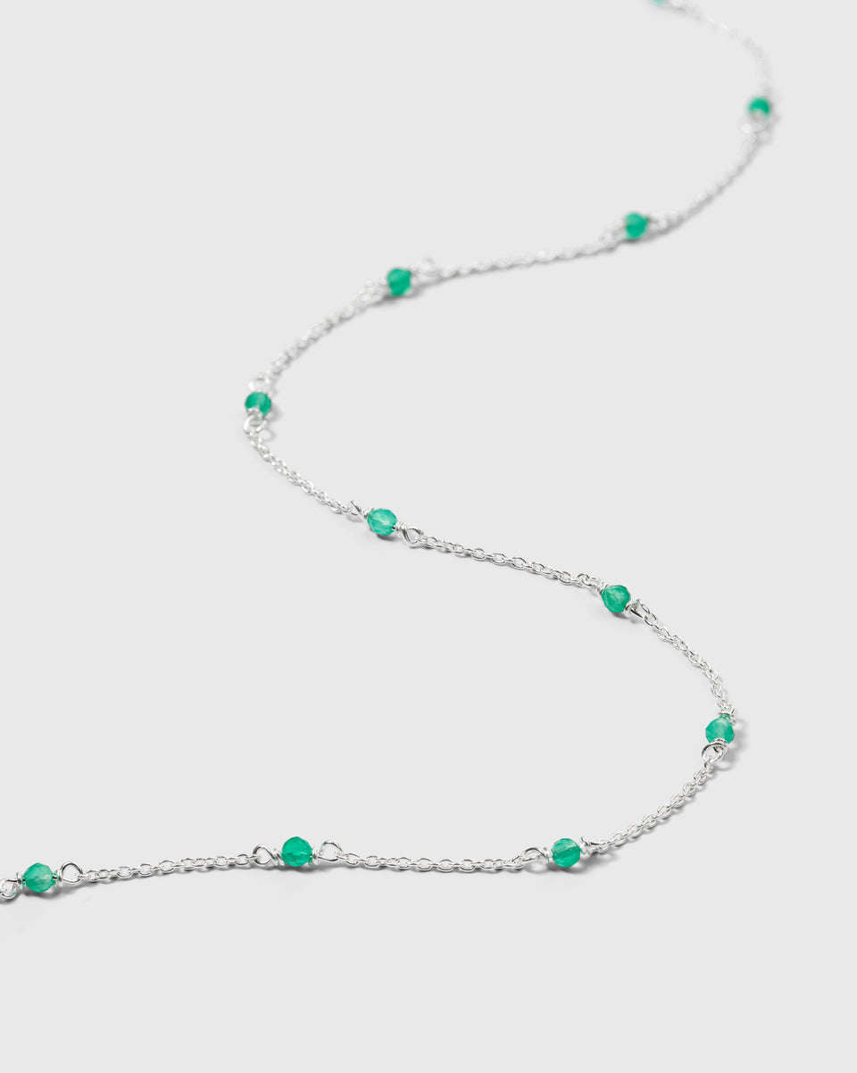 A close-up product shot of the Santa Monica Necklace in silver, laid out to showcase its delicate chain design adorned with small, vibrant green onyx stones.