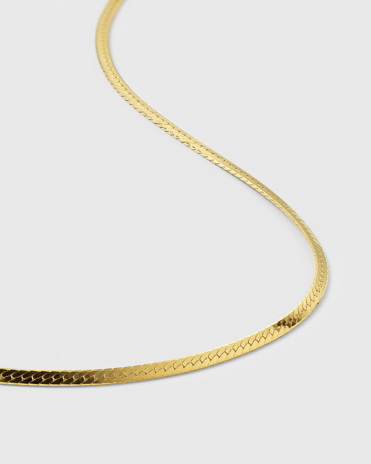 A product shot of the Herringbone Necklace in gold, showcasing its smooth and delicate flat chain design.