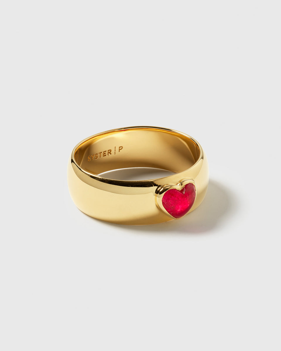 A close-up of the La La Love Ring, a statement piece with a wide, polished gold band and a vibrant pink quartz heart stone set into it.