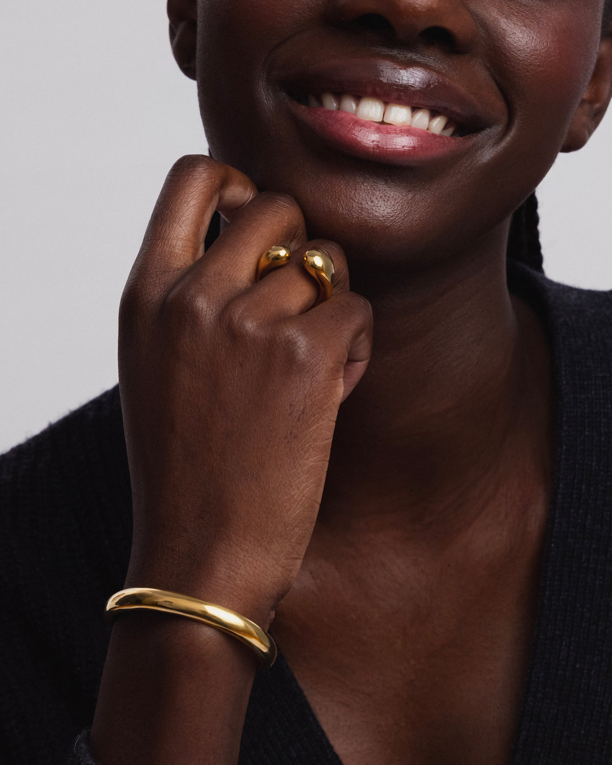 A close-up shot of a model wearing the Bolded Bangle in gold on her wrist, paired with a matching open-ended gold ring with drop-shaped tips on her finger.