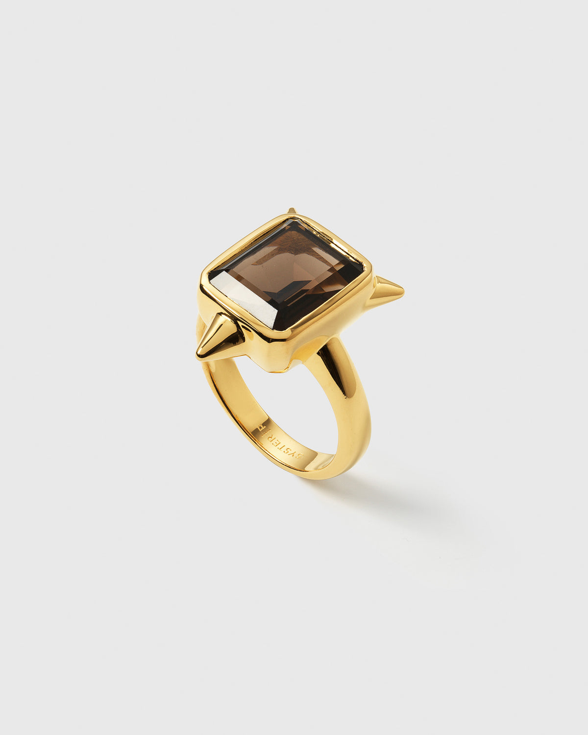 A product shot of the Drama Ring Gold, featuring a large, rectangular smokey quartz set on a gold band with three edgy spikes.