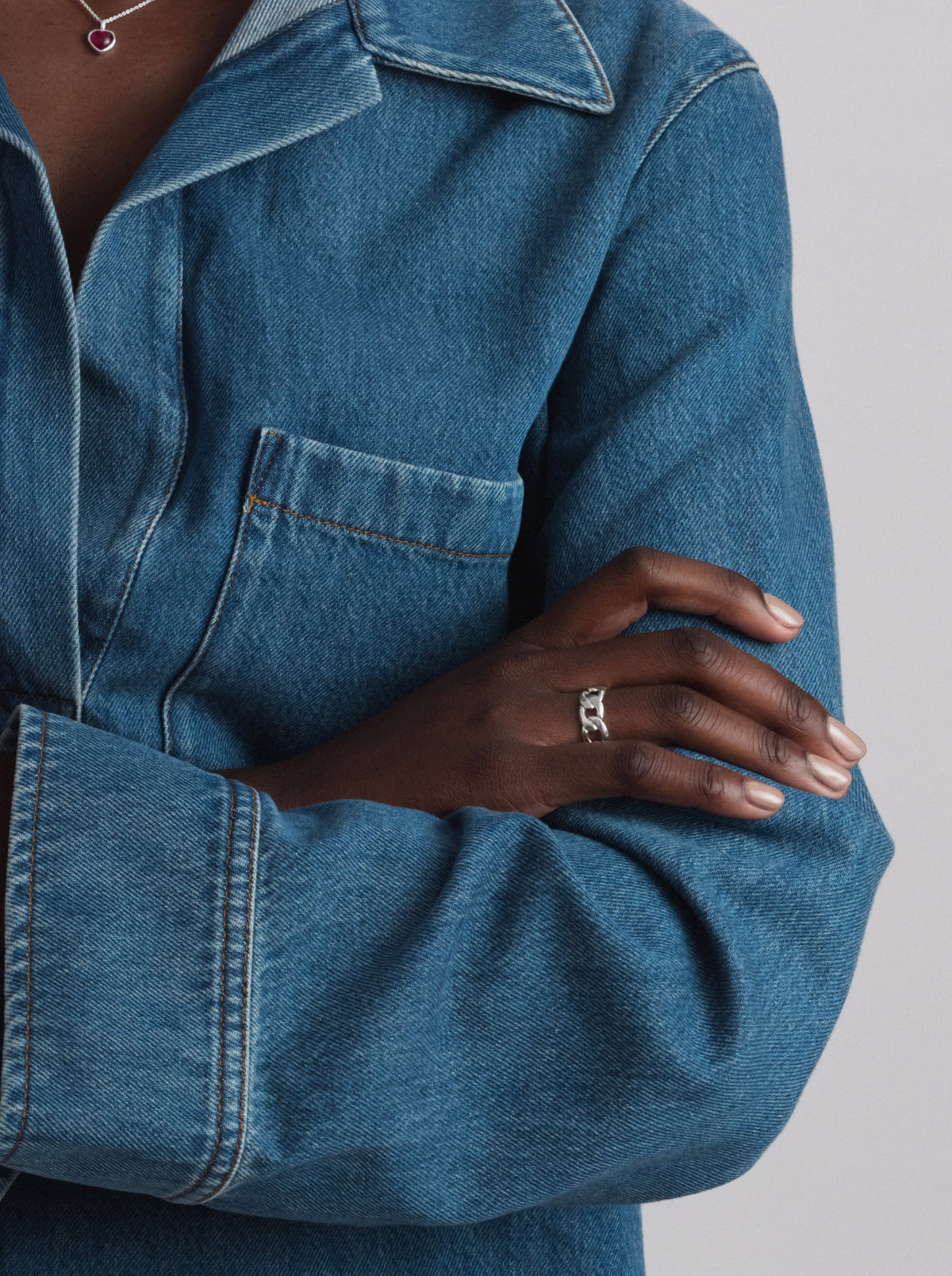 A model wearing the Links Ring in silver, which has a curb chain design, and a silver necklace with a red heart pendant.