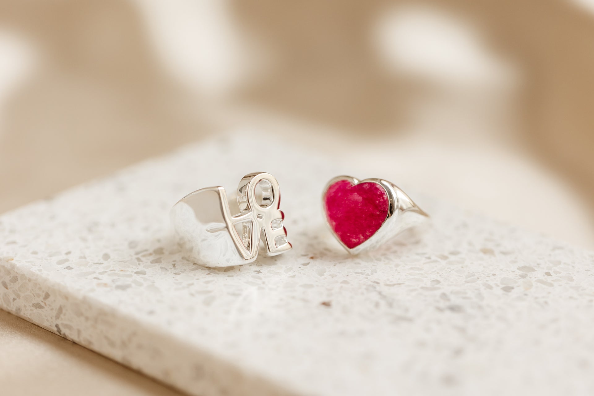 A big silver ring with the word "love" next to silver ring with a big pink quartz heart