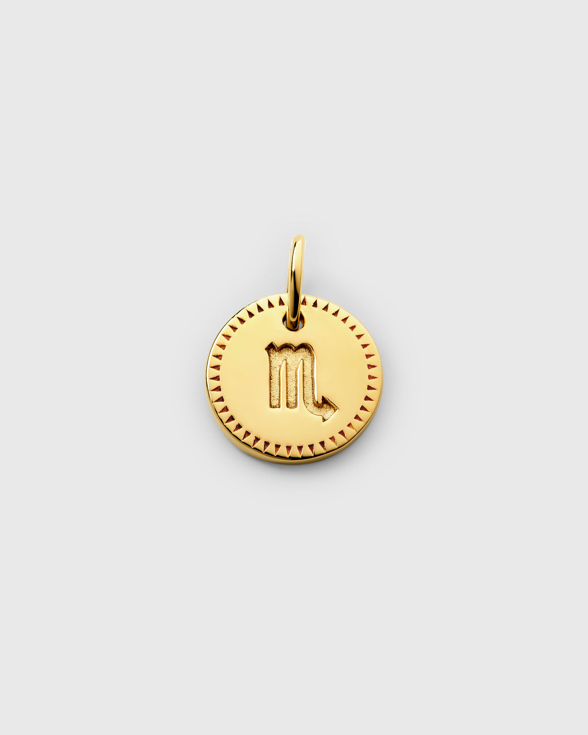 A product shot of the Beloved Zodie Pendant in gold, specifically the Scorpio variant. The round pendant features the engraved Scorpio symbol at its center, framed by a decorative border of small triangles.