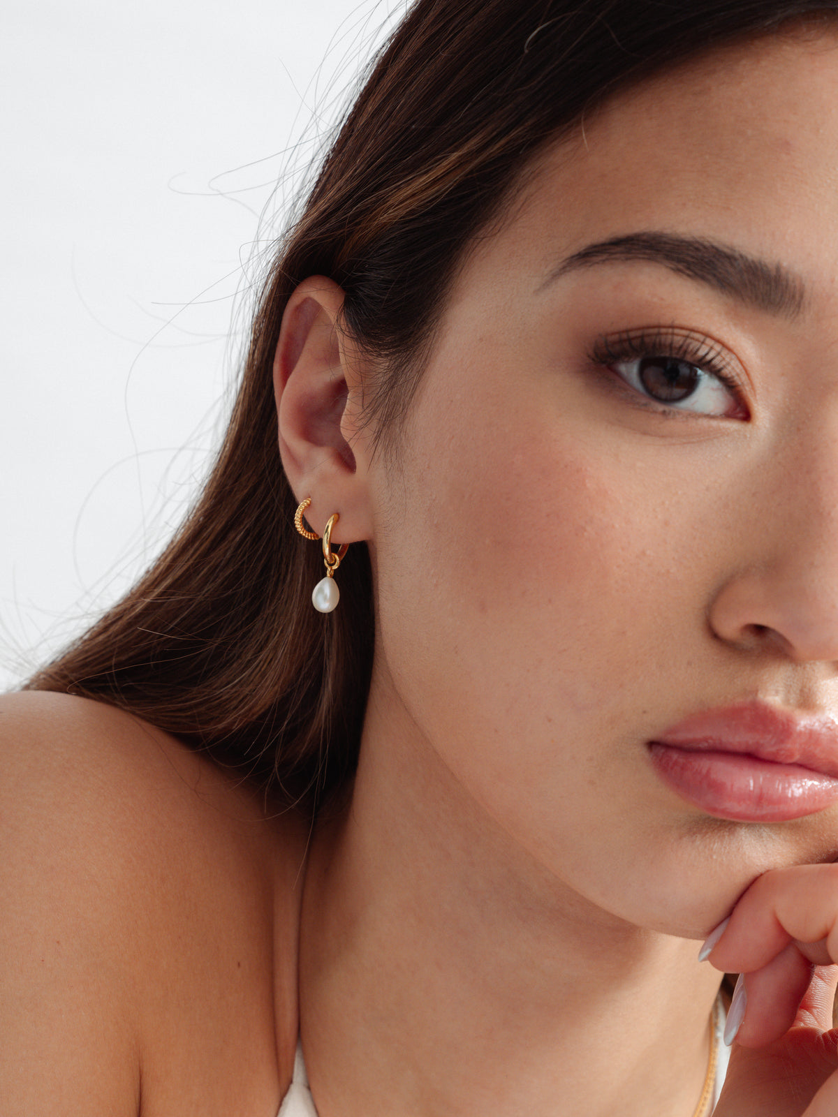 A close-up of a model wearing the Treasure Pearl Hoops Gold, featuring a dangling freshwater pearl, alongside the smaller Beloved Twisted Small Hoops Gold.