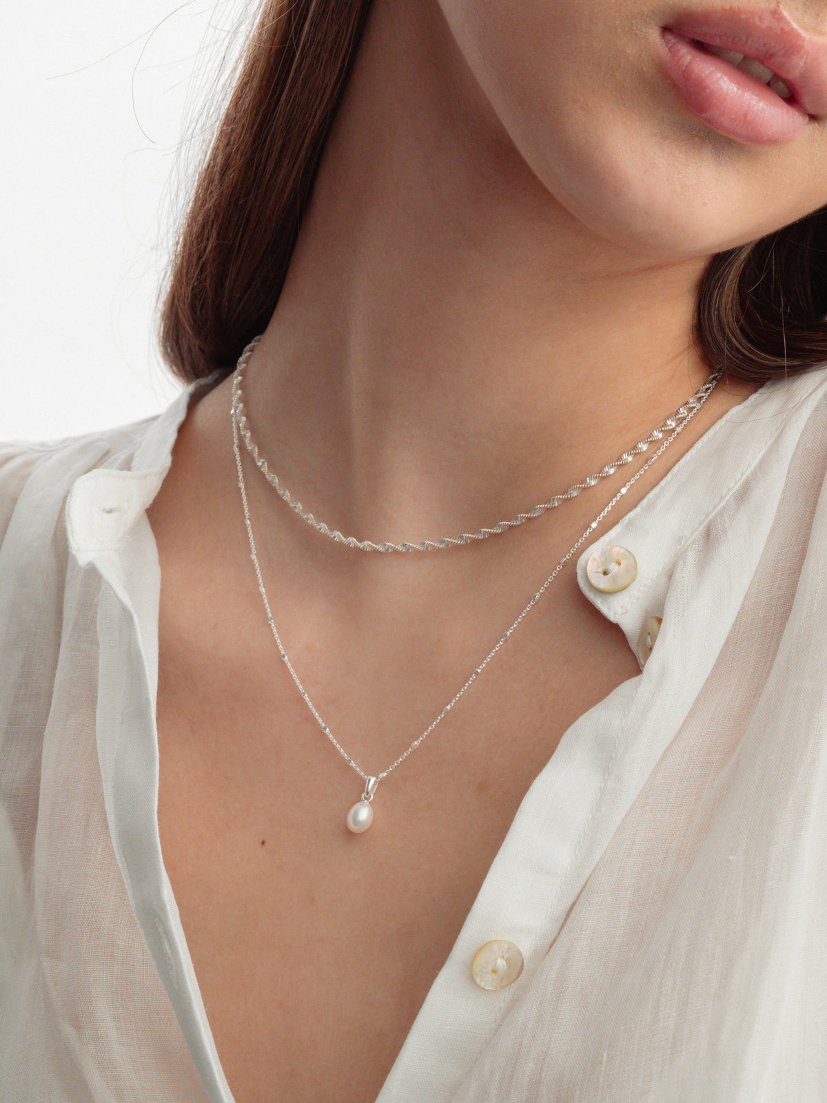 A model wears the Treasure Single Pearl Necklace in silver, featuring a delicate teardrop pearl, layered with the silver Herringbone Twisted Necklace.