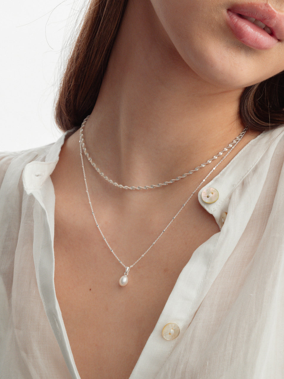 A model wears the Treasure Single Pearl Necklace in silver, featuring a delicate teardrop pearl, layered with the silver Herringbone Twisted Necklace.