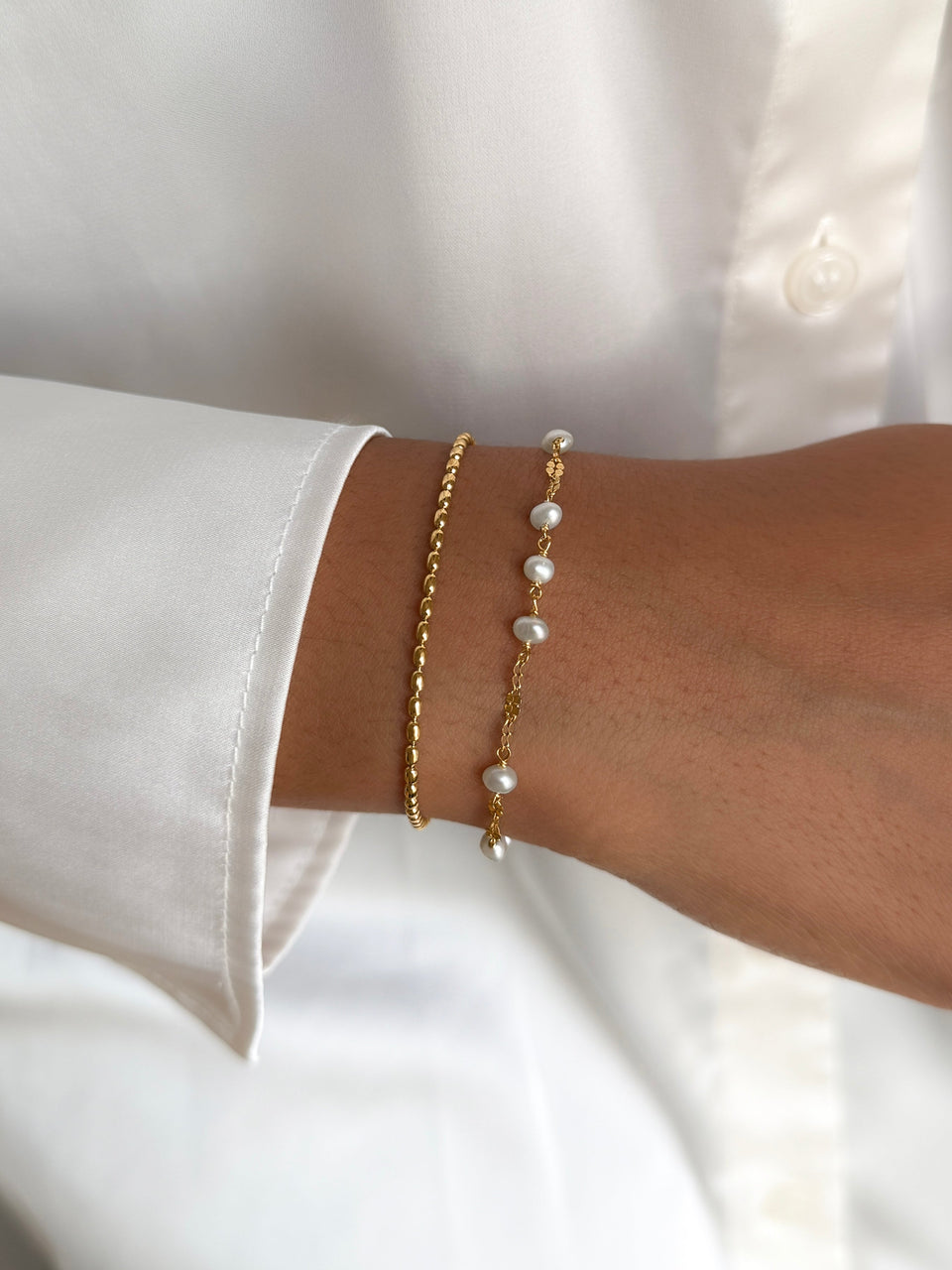 A close-up shot of a model wearing the Aurelia & Lunetta Bracelet Set in gold. The set includes the Lunetta bracelet, a beaded gold chain, and the Aurelia bracelet, a fine gold chain with freshwater pearls.