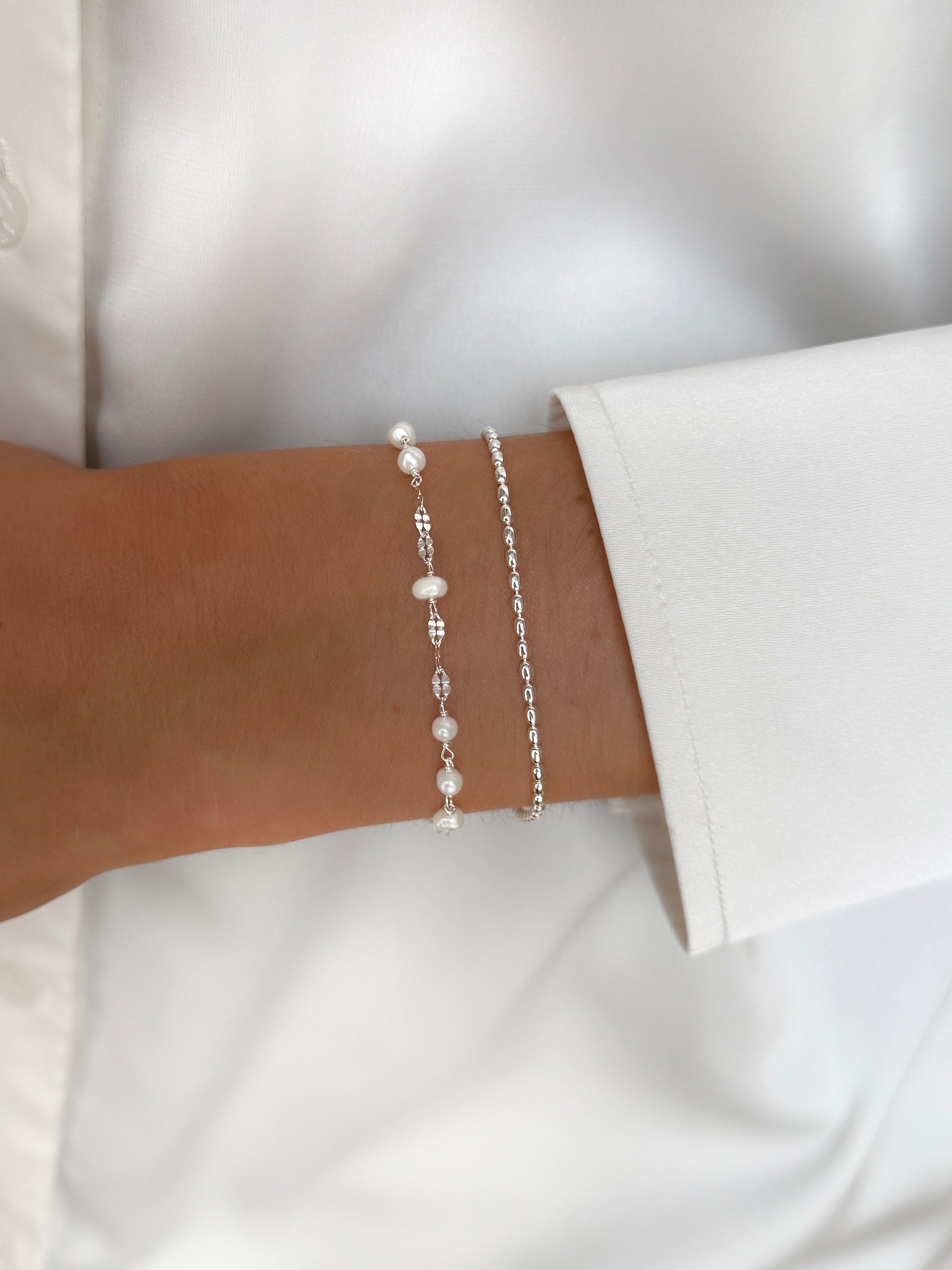 A close-up of a model wearing the Aurelia & Lunetta Bracelet Set in silver, featuring the delicate pearl-adorned Aurelia bracelet stacked with the simple Lunetta chain bracelet.